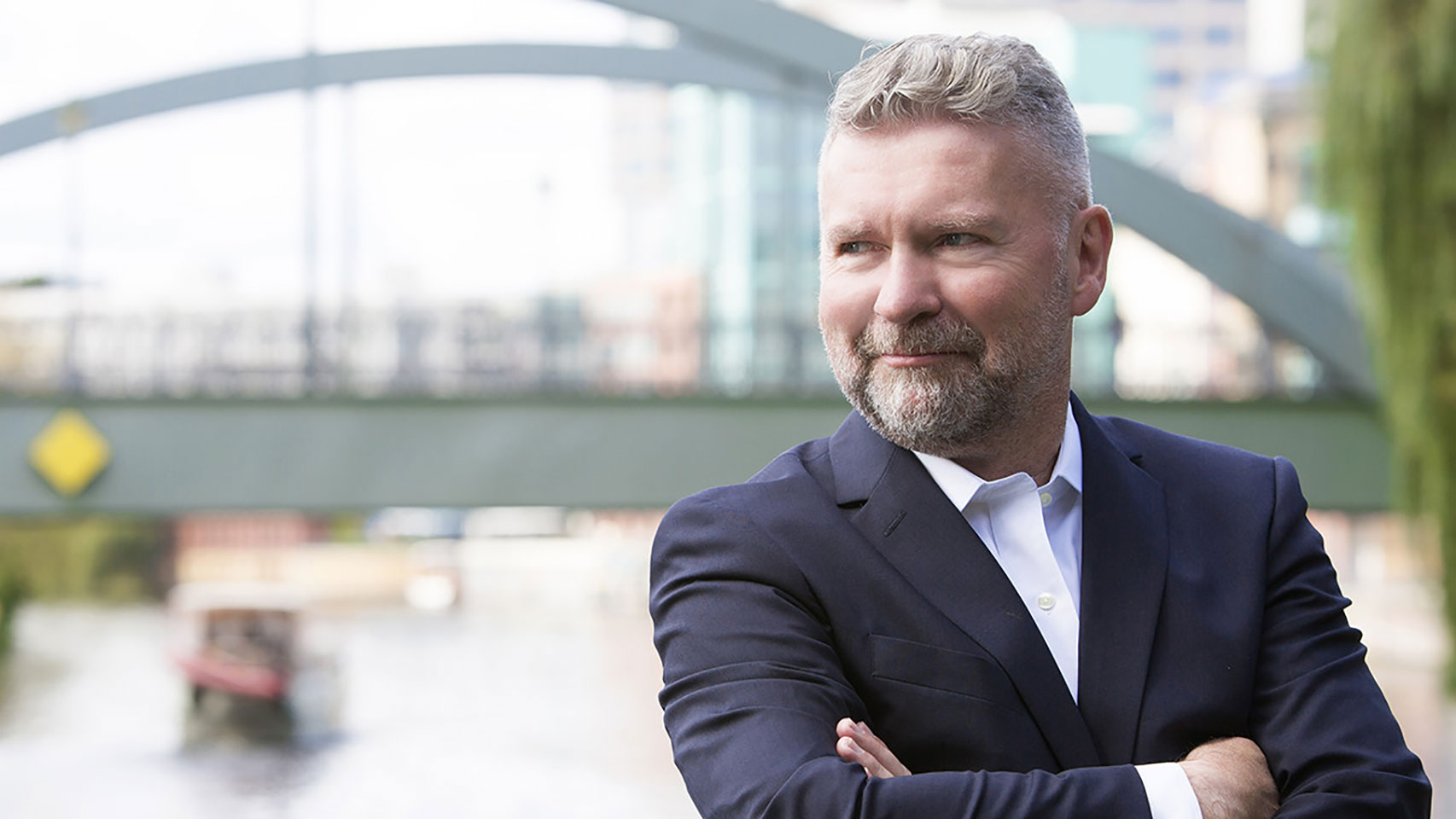 Businessman in a suit with arms folded, looking away from the camera, while outside.