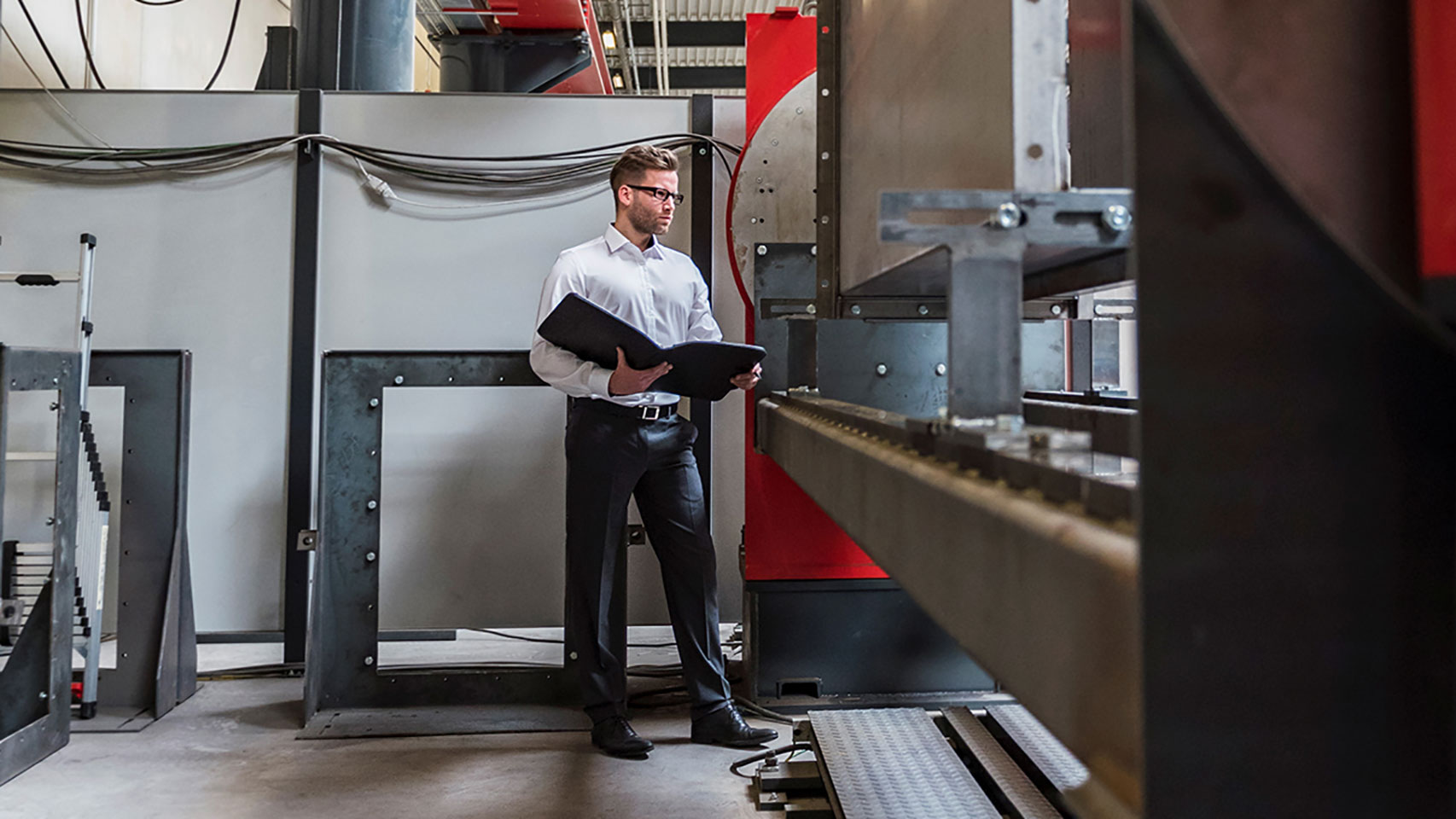 Man in a warehouse reviewing plans vs. a machine he's looking at.