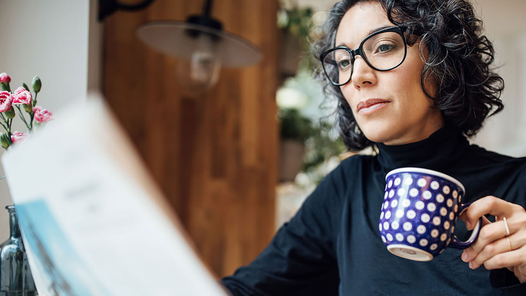 Woman holding a coffee cup and looking at a newspaper