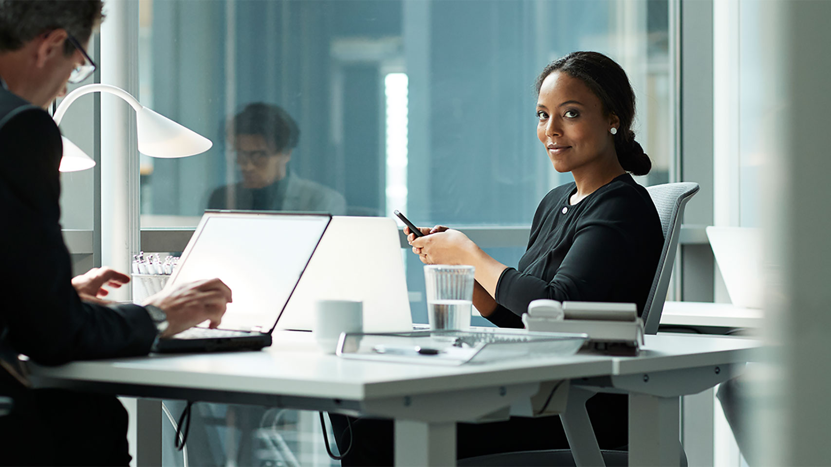 Businesswoman at a table holding a cell phone and subtly smiling at the camera