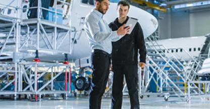 Two in an airplane hanger men looking at a tablet