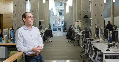 Man in an open office setting smiling while looking away from the camera