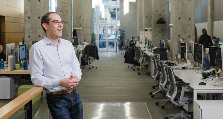 Man in an open office setting smiling while looking away from the camera