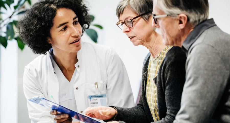 Woman doctor sitting down and showing a medical chart to an elderly couple.