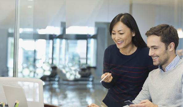 Two business people smiling and working on something together at a shared desk