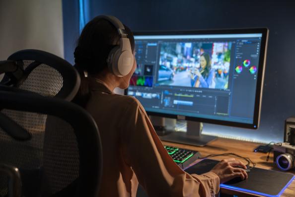 Woman sitting at a computer wearing headphones using video editing software